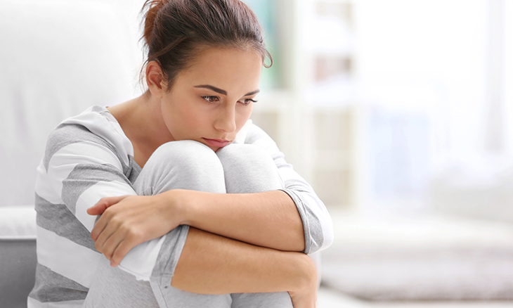 Depressed young woman sitting on floor at home